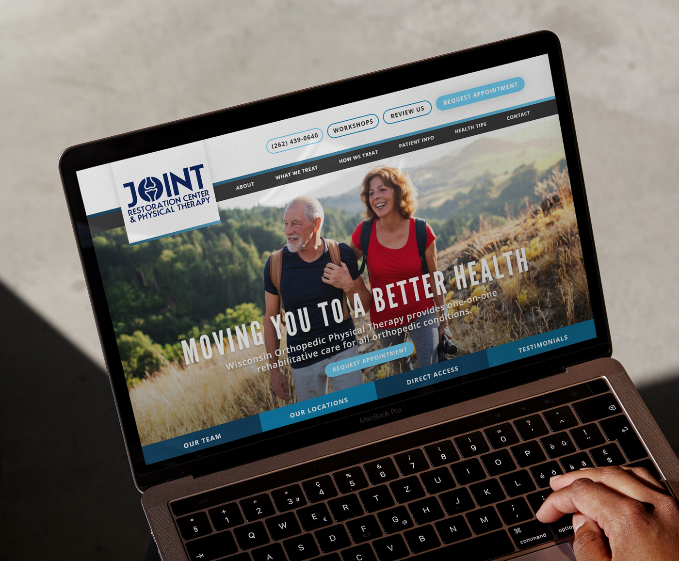 A laptop screen showing the homepage of Joint Restoration Center & Physical Therapy. The site features a large image of an older couple hiking, with bold white text reading “Moving You to a Better Health.” Navigation options and call-to-action buttons are visible at the top and bottom of the screen.